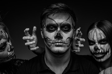 Male and female face art for Halloween. Black and white portrait of a guy and two girls with scary painted faces on a black background. All saints ' night.