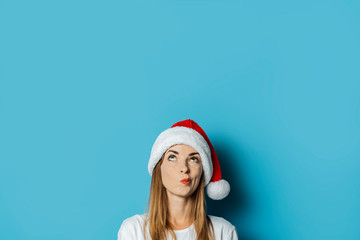 Young woman in Santa Claus hat with a mysterious face on a blue background. Concept idea for new year and christmas