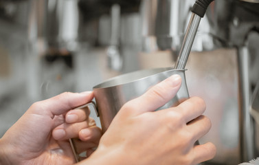 hands Barista steaming milk in pitcher.preparing steam milk by coffee machine to make latte art in cafe.latte is a coffee drink made from espresso and steamed milk.cup of latte coffee.