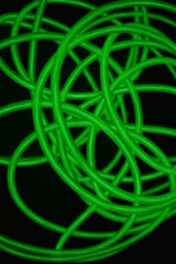 Toxic green luminous wires with different shapes and structures. A web of lime fiber and unusual circles located on a black glossy surface.