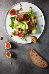 Green salad with figs on white plate and grey background. Top view shot.