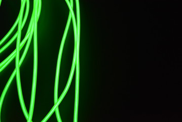 Toxic green luminous wires with different shapes and structures. A web of lime fiber and unusual circles located on a black glossy surface.