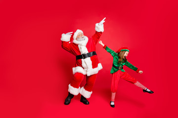 Full size photo of excited santa claus and elf in hat with eyeglasses eyewear dancing fooling wearing bright costumes isolated over red background