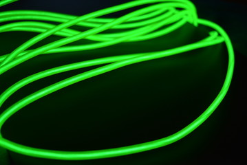 Toxic green luminous wires with different shapes and structures. A web of lime fiber and unusual circles located on a black glossy surface.