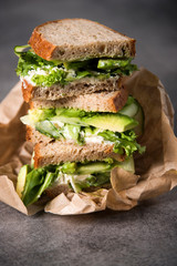 Three sandwiches on top of each other. Layered rustic breads with avocado and fresh salad on grey background.