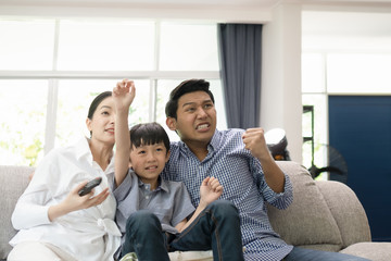 young family, father, mother and son watching TV feeling exciting together in living room, happy family concept