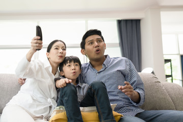 young family, father, mother and son watching TV feeling exciting together in living room, happy family concept