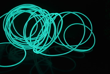 Unusual bright wires made of turquoise-colored material glowing at night. Chaotic sky blue wires, light guide electroluminescent wires, electroluminescence are located on a glossy black surface.