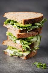 Three sandwiches on top of each other. Layered rustic breads with avocado and fresh salad on grey background.