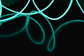 Unusual bright wires made of turquoise-colored material glowing at night. Chaotic sky blue wires, light guide electroluminescent wires, electroluminescence are located on a glossy black surface.