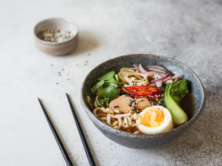 Asian Ramen noodles with chicken, pak choi cabbage and egg on grey background. Copy space