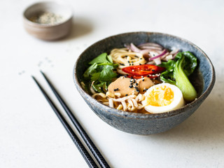 Asian Ramen noodles with chicken, pak choi cabbage and egg on grey background. Copy space