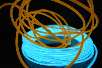 A bright coil of turquoise, sky blue luminous wire with chaotic wires of an orange light guide located on a black glossy surface. Light canvas, backlighting with wires and art background.