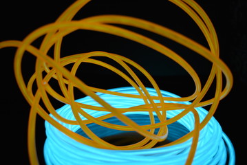 A bright coil of turquoise, sky blue luminous wire with chaotic wires of an orange light guide located on a black glossy surface. Light canvas, backlighting with wires and art background.