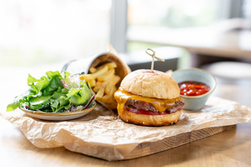 Cheeseburger with lettuce, tomato, fries, and melted cheese. The table in the restaurant. Unhealthy food.