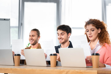 three smiling friends sitting at table and doing paperwork