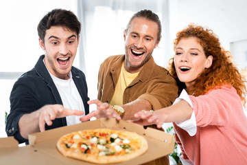 selective focus of three smiling friends taking pizza from box