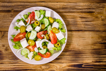 Ceramic plate with greek salad on wooden table. Top view