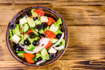 Ceramic plate with greek salad on wooden table. Top view