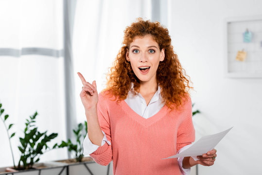 attractive and shocked businesswoman showing idea sign and holding paper