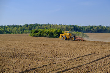 A farm tractor cultivates land after harvesting grain.