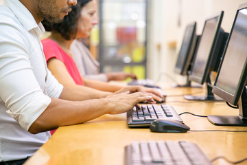 Multiethnic group of students working in computer class. Row of man and women in casual sitting at table, using desktops, typing. Training center concept