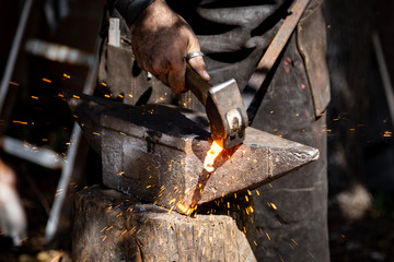 The blacksmith manually forging the molten metal on the anvil in smithy with spark fireworks - obrazy, fototapety, plakaty