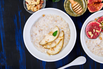 A bowl of porridge with pears slices and walnuts and porridge with figs on dark blue background. Two bowls. Flat lay. Copy space. Top view.