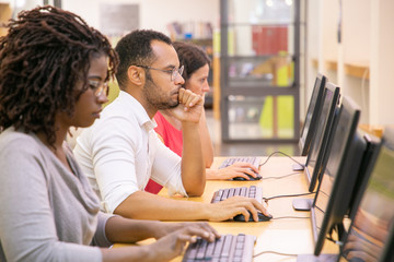 Multiracial group of students training in computer class. Line of man and women in casual sitting...
