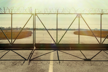 The fence with barbed wire. The road leading to the closed gate, a dead end.