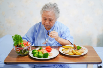 Asian senior or elderly old lady woman patient eating breakfast healthy food with hope and happy while sitting and hungry on bed in hospital..