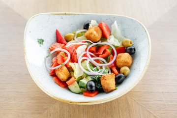 Traditional greek salad with fresh vegetables, feta cheese and olives. Wooden table in restaurant