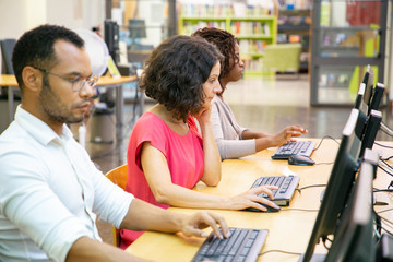Diverse adult students working in computer class. Line of man and women in casual sitting at table,...