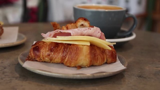 Freshly baked croissant with cheese and ham on a ceramic plate with lat on a table in a cafe.