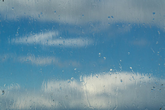 beautiful clouds behind wet rainy glass with droplets