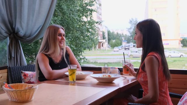 Two friends in a cafe-bar drink cocktails on an open terrace.