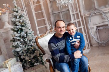 Cheerful bald dad with his son in sweaters waiting for the New Year against the background of the Christmas Tree.