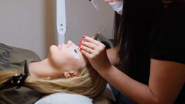 Woman Eye with Long Eyelashes. Eyelash Extension. Lashes, close up, selected focus. Gluing artificial eyelashes with tweezers. Beautician in magnifier glasses performs laborious small work.