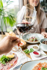 Date, man and woman Clink wine glasses. Beautiful young elegant woman in the restaurant with a wine glass. Dinner and a variety of dishes on the table. Italian cuisine
