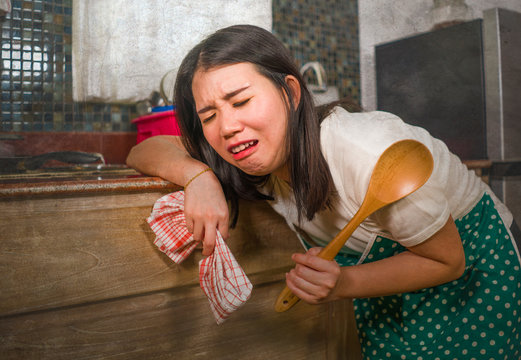 young tired and stressed Asian Korean woman in cook apron working leaning on kitchen sink lazy in moody and upset face housekeeping at home and crying