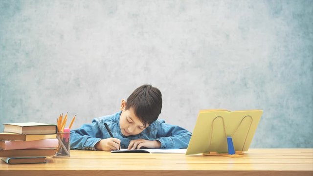 Young clever school kid in blue jeans t-shirt was writing, finished his homework and now satisfied with the result.
