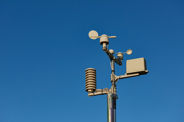 A small Amateur Weather Outdoor forecasting Station with rainfall gauge, thermometer, Anemometer and wind direction instruments on a metal pole.