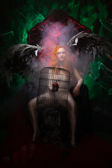 an evil tempting woman with large demon wings holds an Apple in a large cage and beckons to sin....