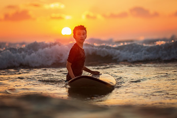 Side view of fearless kid floating surfboard at ocean with waves on sunny evening