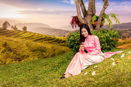 Beautiful Vietnamese Girl sitting on green lawn and golden terraced rice fields background..