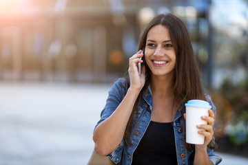 Young woman with smartphone and coffee in the city 