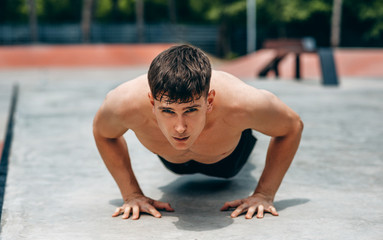Fototapeta premium Image of young athletic muscular man doing push-ups on workout ground. Caucasian fitness male doing workout exercises on sunset light background. People and sport concept