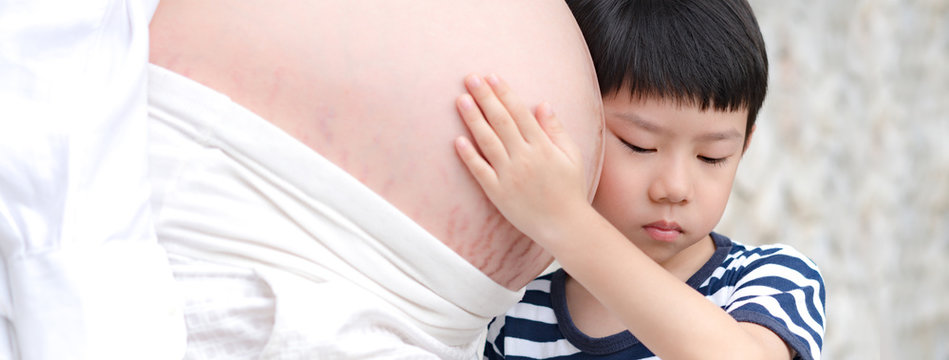 Close up banner picture of a cute little asian boy who expecting to be big brother touching his mommy's belly and feel the baby inside. Third trimester prenatal, Miracle of life, Precious moment.