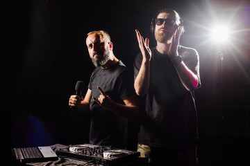 DJ plays on a mixer and presenter with microphone in the club on black background