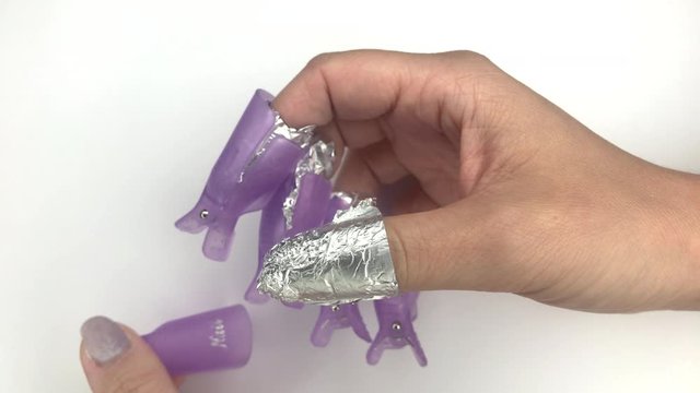 Putting off plastic reusable cap clip for soak-off UV gel polish removal. Womens nails wrapped in cotton pads soaked in acetone and aluminium foil. Manicure process, removing gel nail polish.